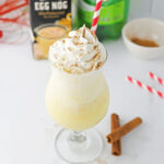 A glass of eggnog with cinnamon and whipped cream.