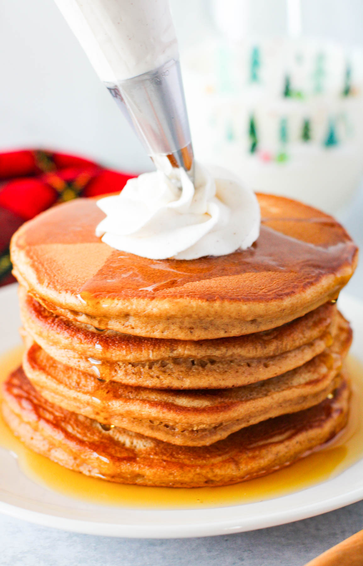 A stack of pancakes being topped with whipped cream.