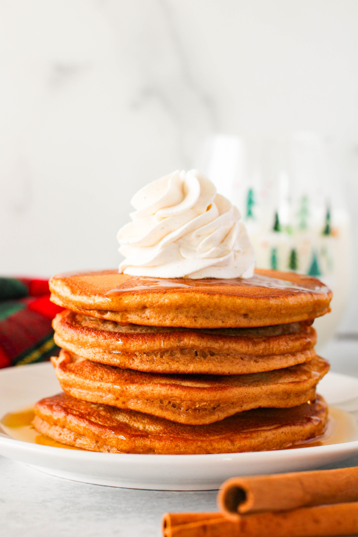 A stack of pancakes with whipped cream and cinnamon sticks.