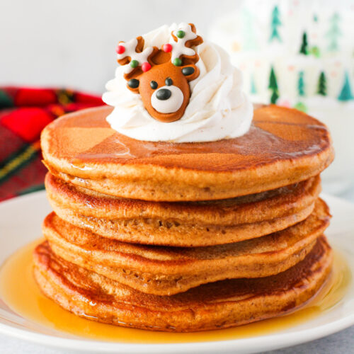 A stack of pancakes with whipped cream and reindeer on top.