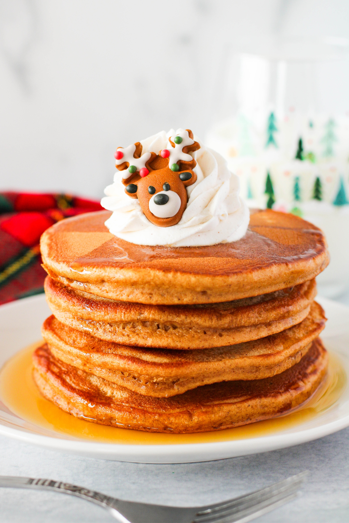 A stack of pancakes with whipped cream and reindeer decorations.