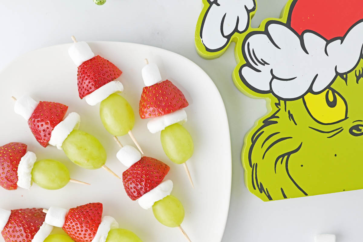 A plate of grapes and strawberries with a santa hat on it.