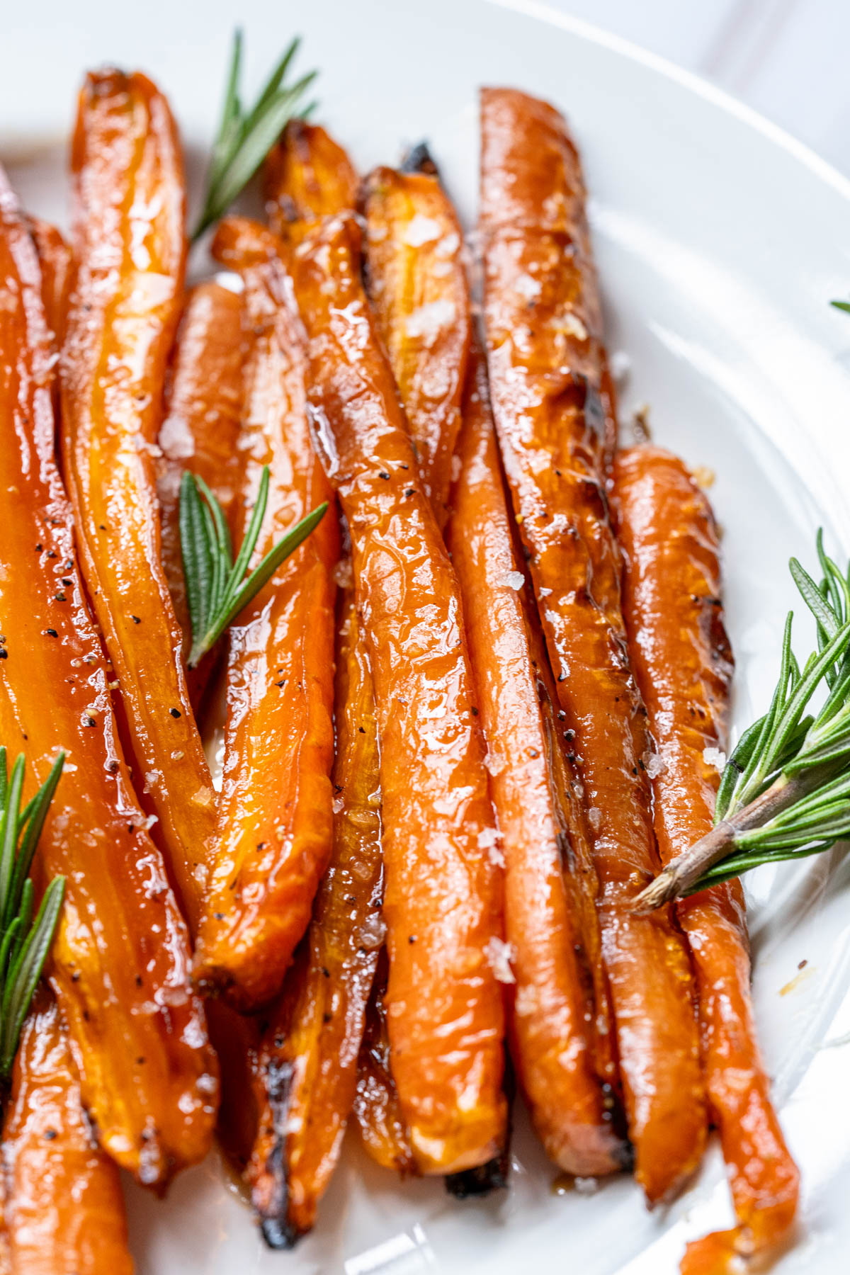 Roasted carrots on a white plate with rosemary sprigs.