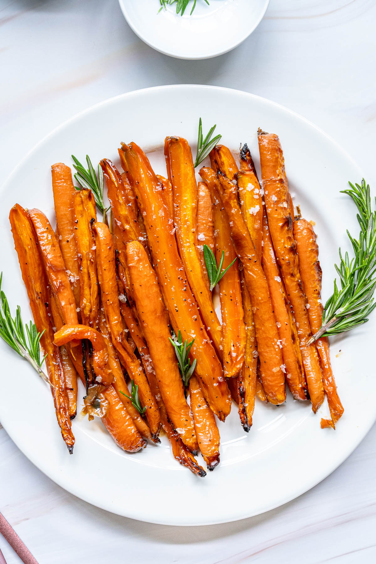 Roasted carrots on a white plate with rosemary sprigs.