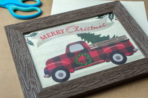 A framed christmas card with a truck and a christmas tree.