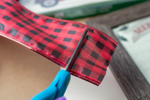 A pair of scissors is being used to cut a piece of plaid fabric.
