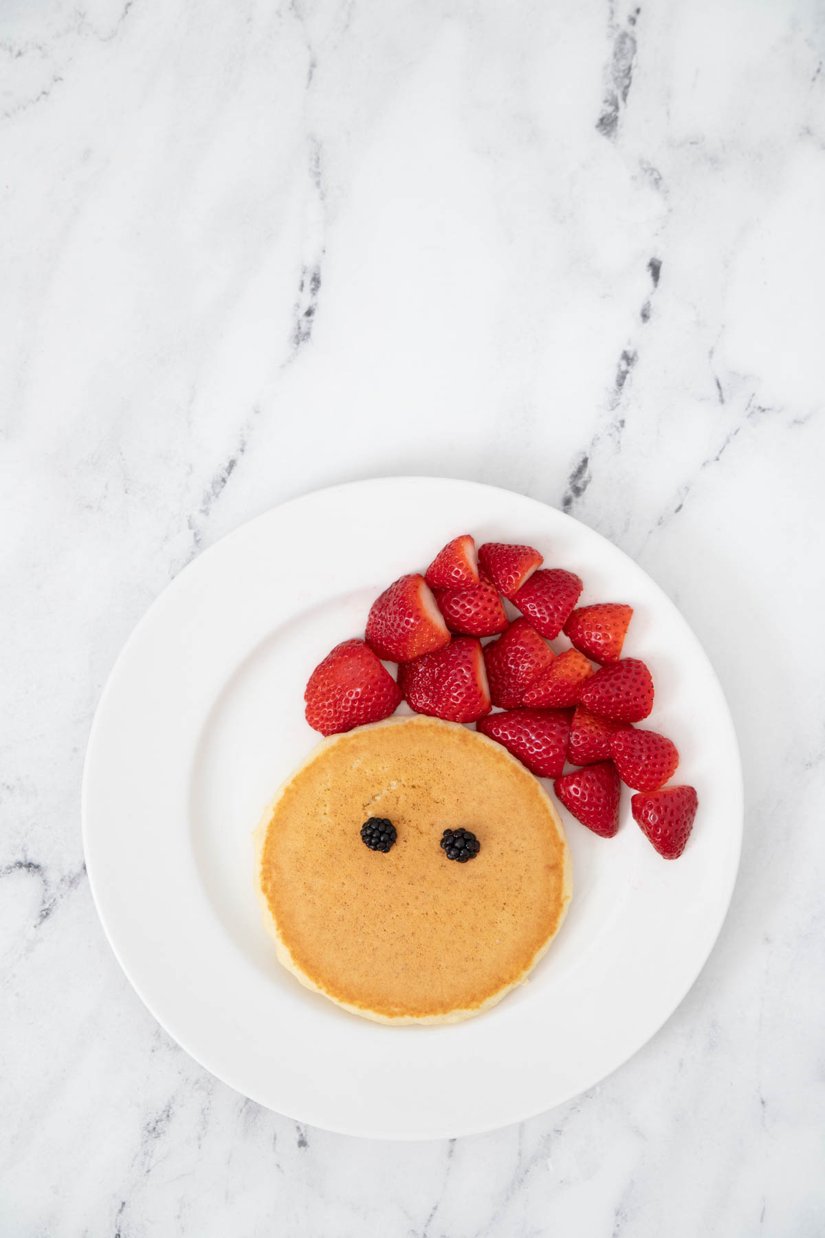 A plate of pancakes with strawberries and a face on it.