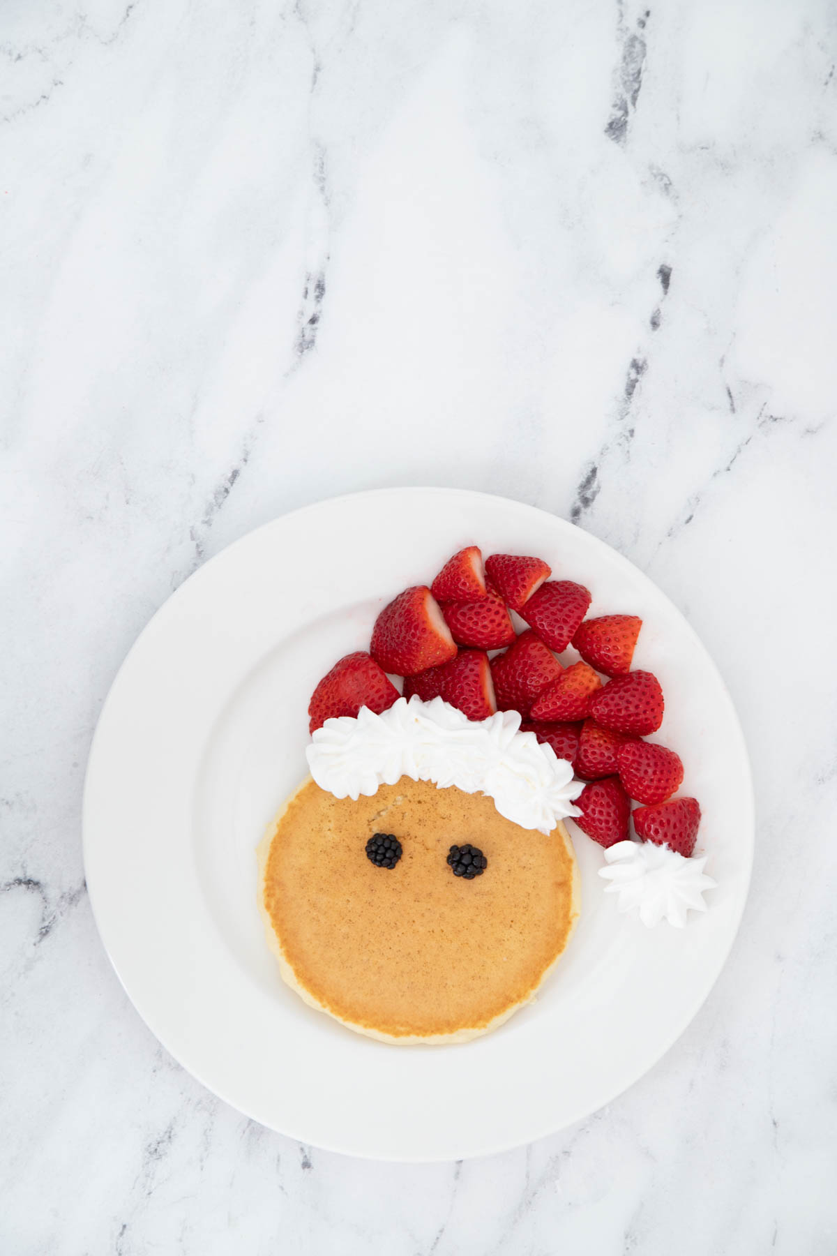 A plate of pancakes with strawberries and a santa hat on it.
