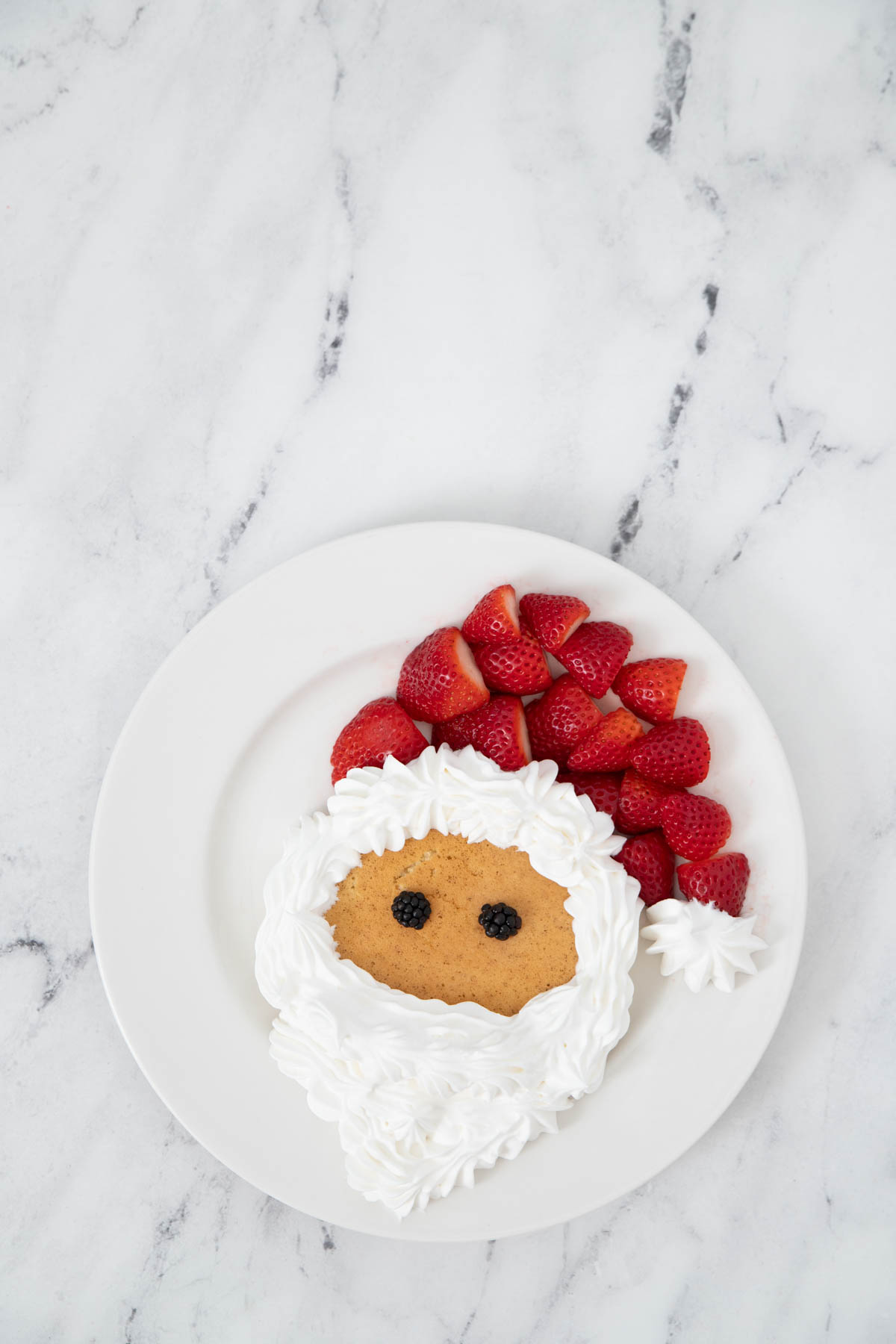 A plate with a santa claus shaped pancake and strawberries.