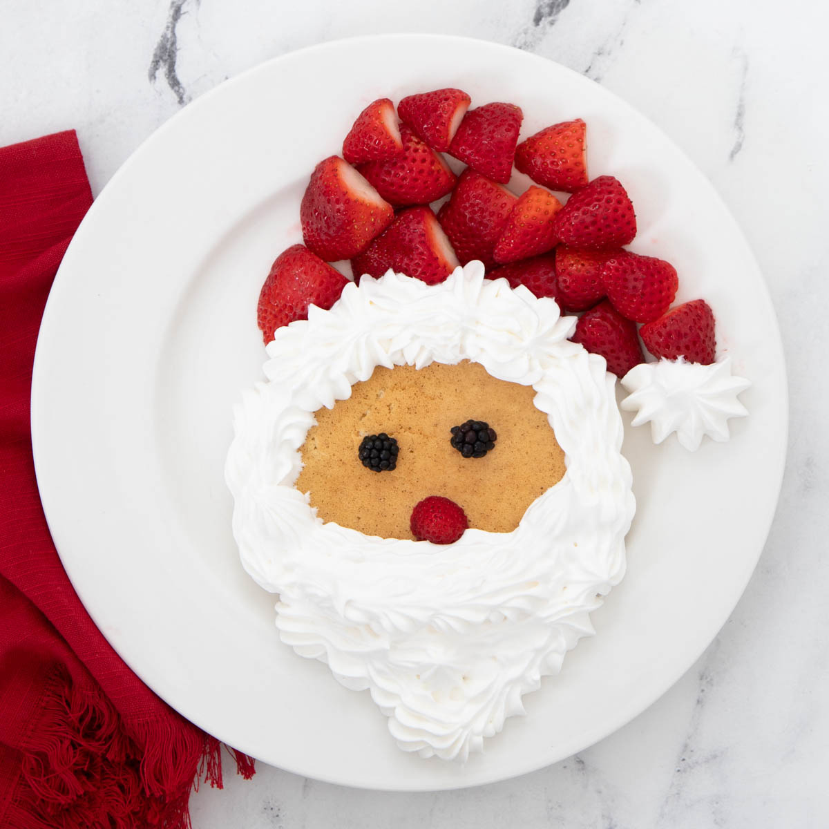 A plate with a santa face pancake and strawberries on it.