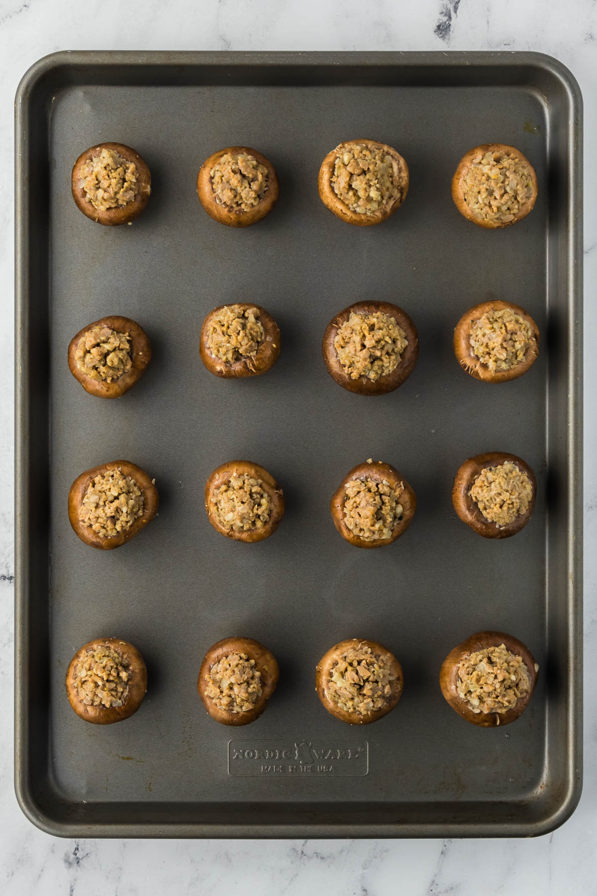 A baking sheet filled with stuffed mushrooms on a marble countertop.