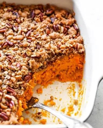 Sweet potato casserole in a white dish with a spoon.