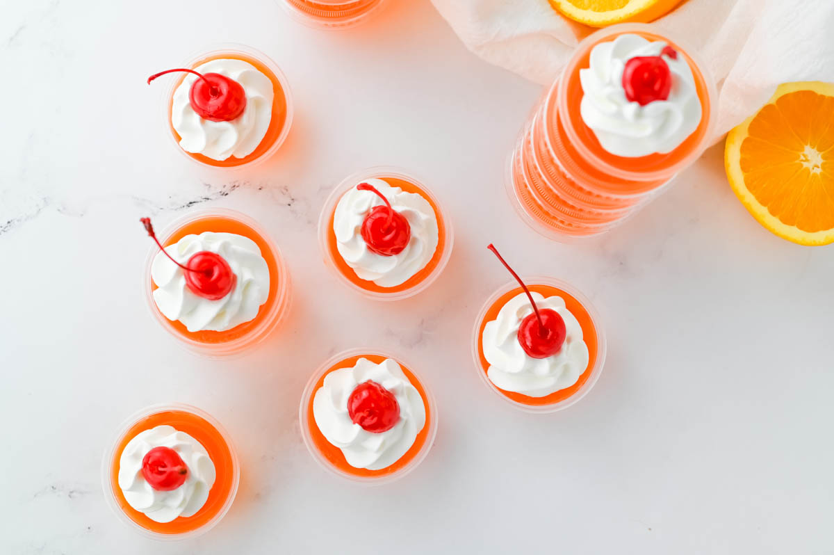 A group of bahama mama jello shots with whipped cream and cherries.