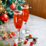 Two champagne cocktails on a table with Christmas decorations.