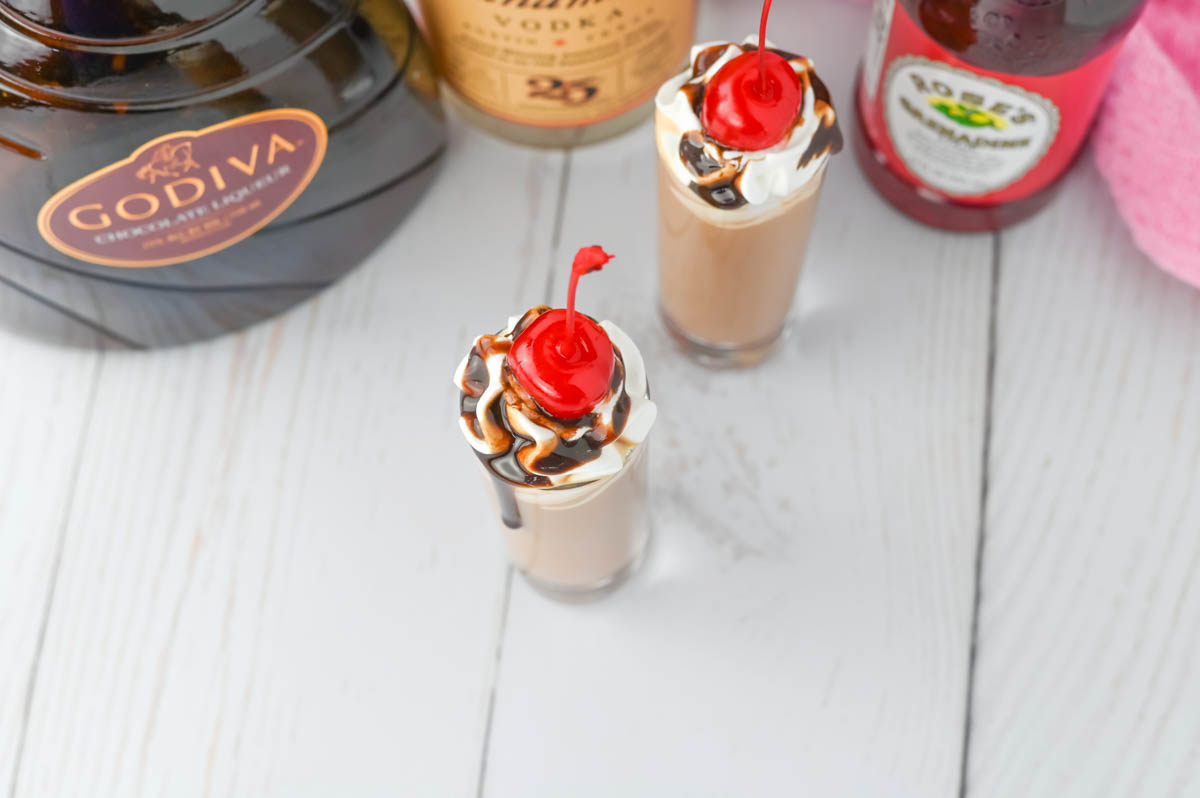 A chocolate shot with whipped cream and a cherry on top.