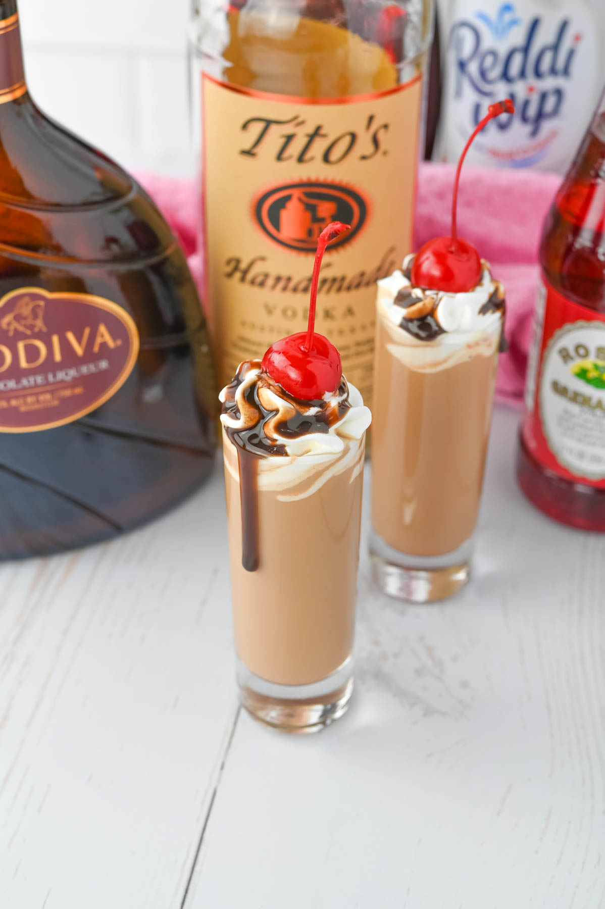 Two chocolate covered cherry shots with whipped cream and a bottle of tito's.