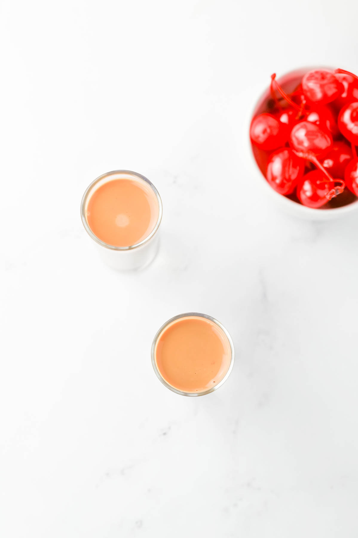 Chocolate cherry shots and a bowl of red cherries on a white table.