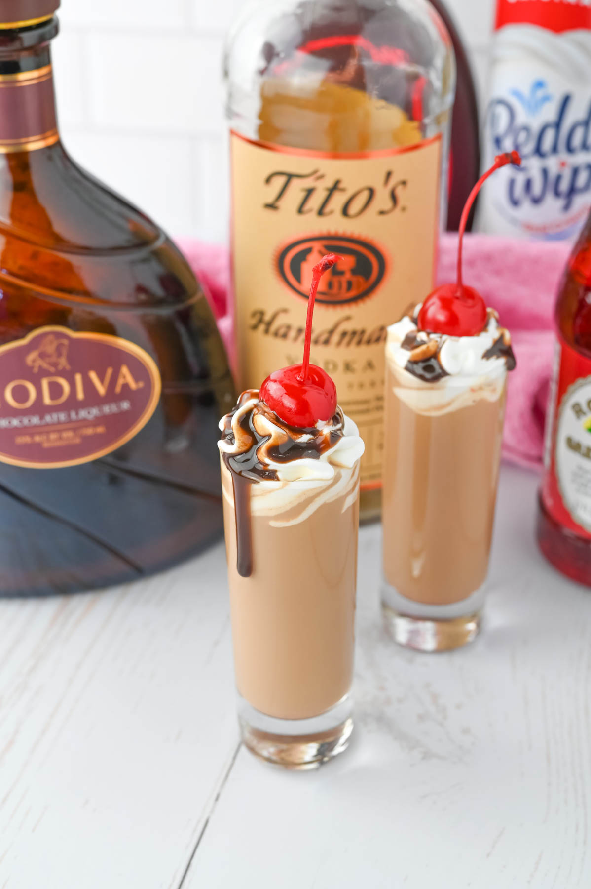 Two glasses with whipped cream and a bottle of tito's.