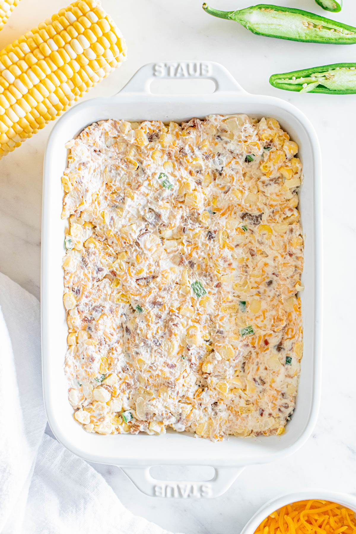 Cheesy corn casserole in a white dish with corn on the side.