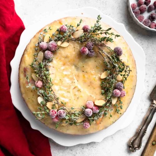 A cake topped with cranberries and sprigs of thyme.