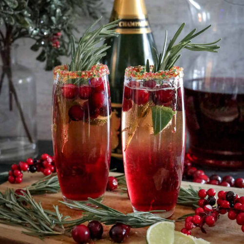 Two glasses with cranberries and rosemary on a cutting board.