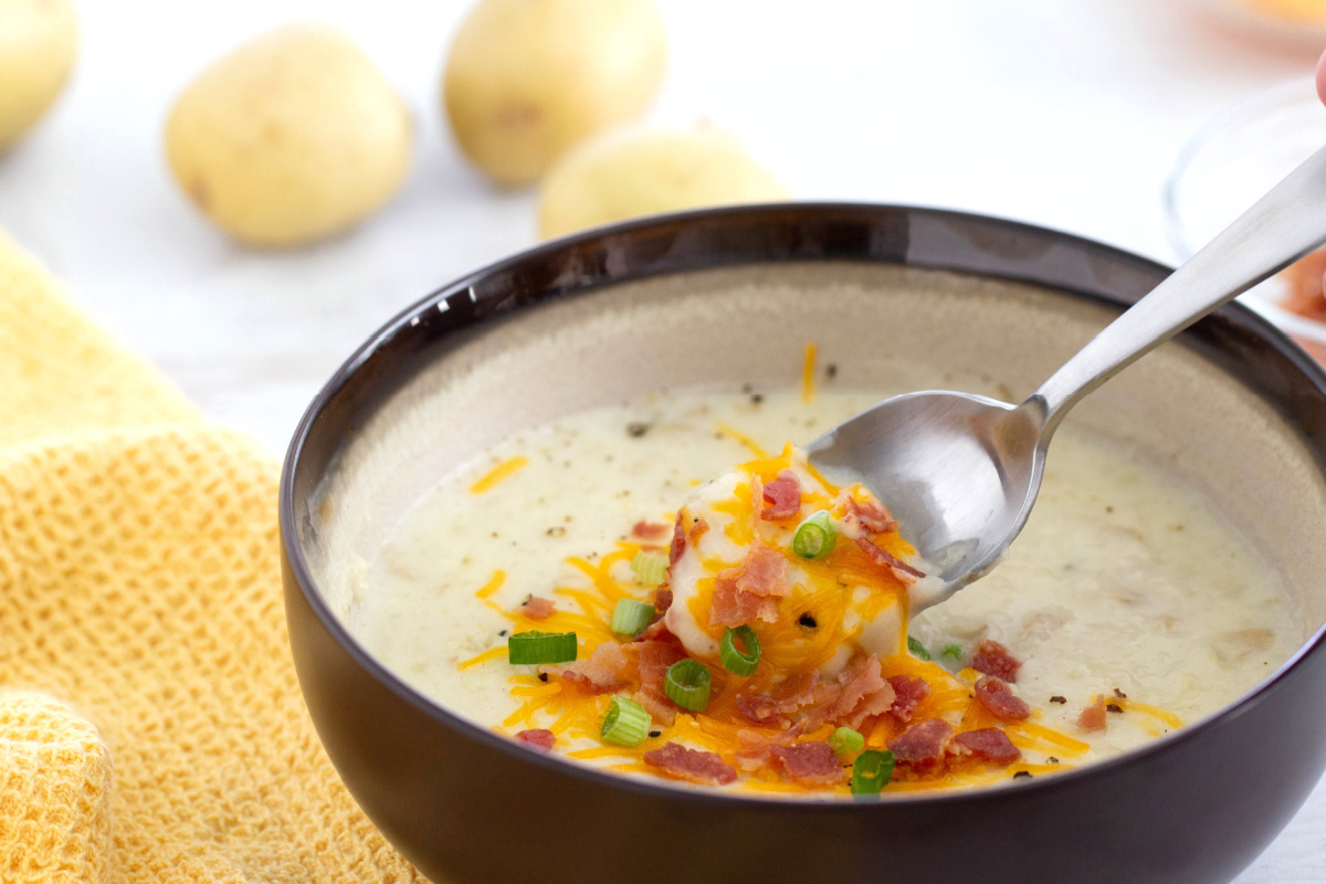 A spoon full of cheesy potato soup with bacon and cheese.