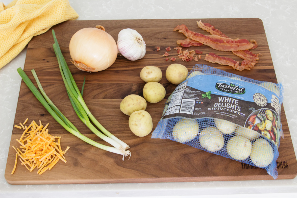 A cutting board with bacon, onions and potatoes.