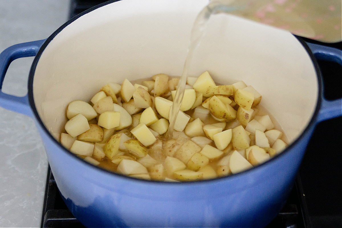 A blue pot with chicken broth being poured over potatoes