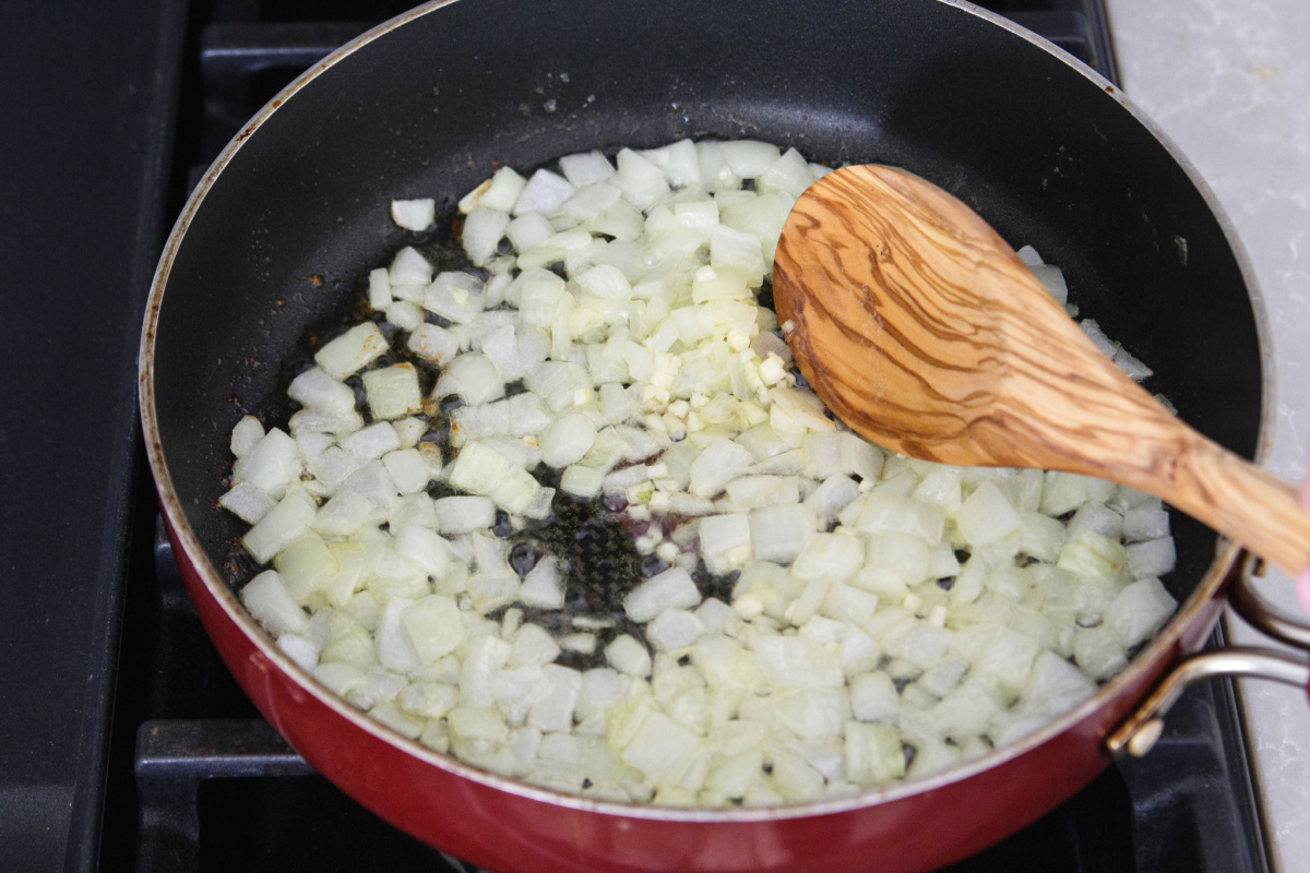 Onions in a pan with a wooden spoon.