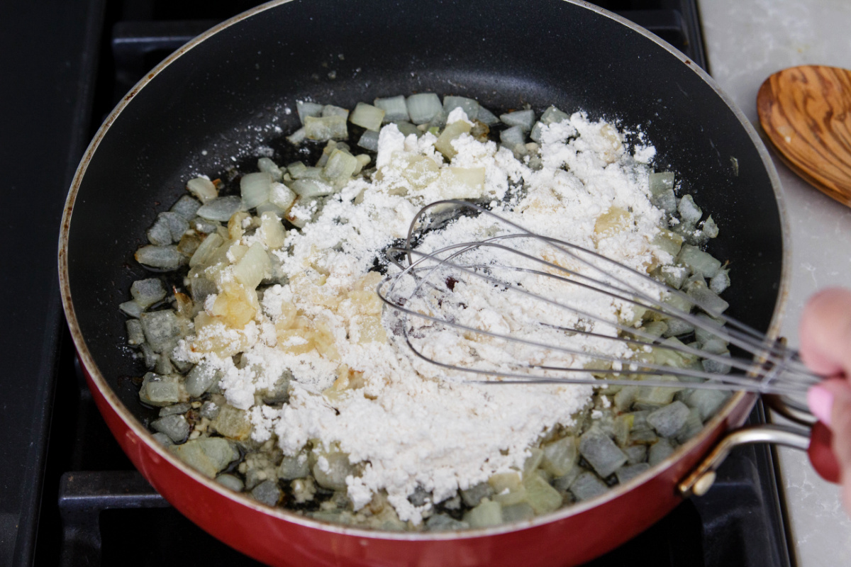 A person whisking flour and onions in a pan.