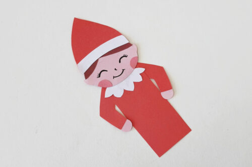 An elf paper cut out on a white surface.