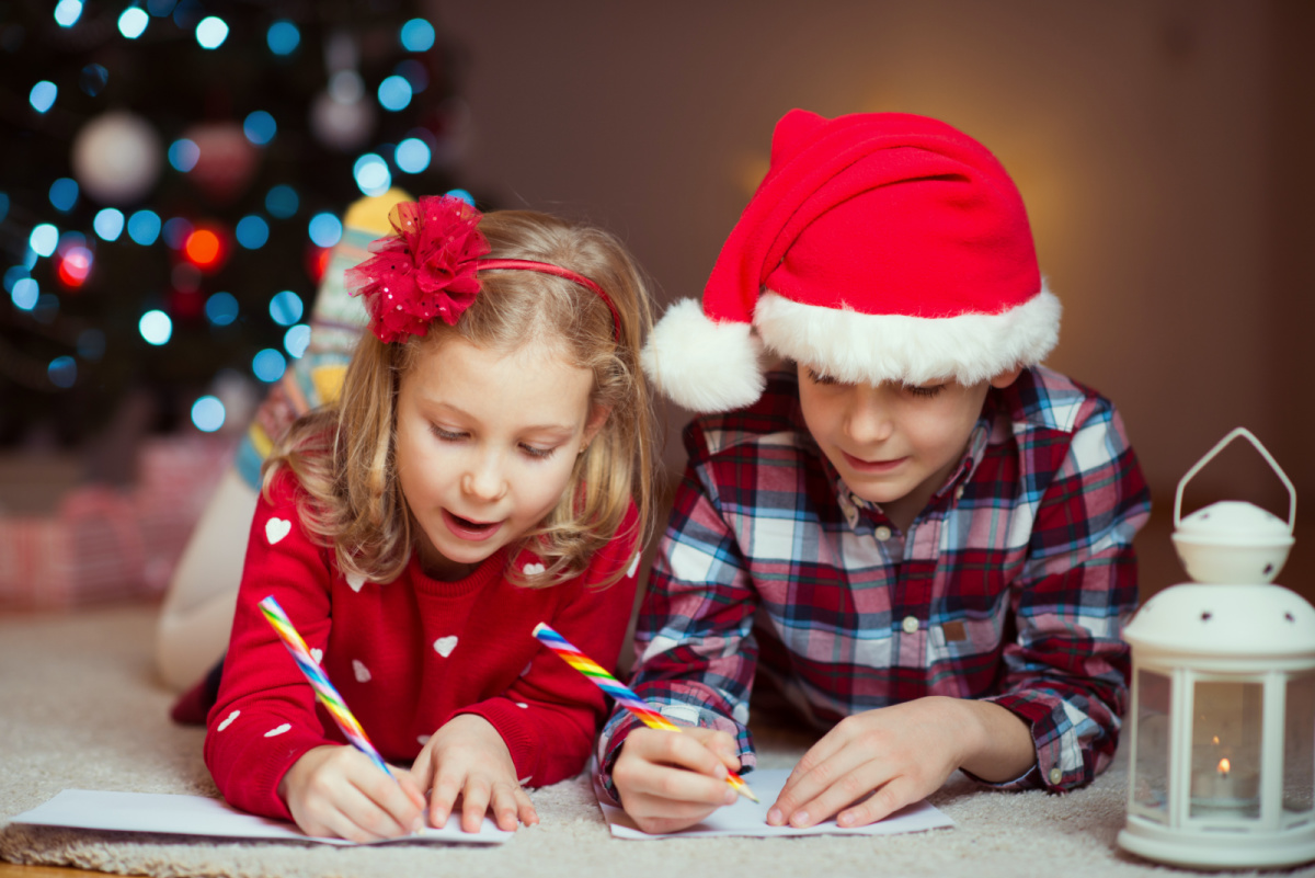 Two children in santa hats writing on the floor.
