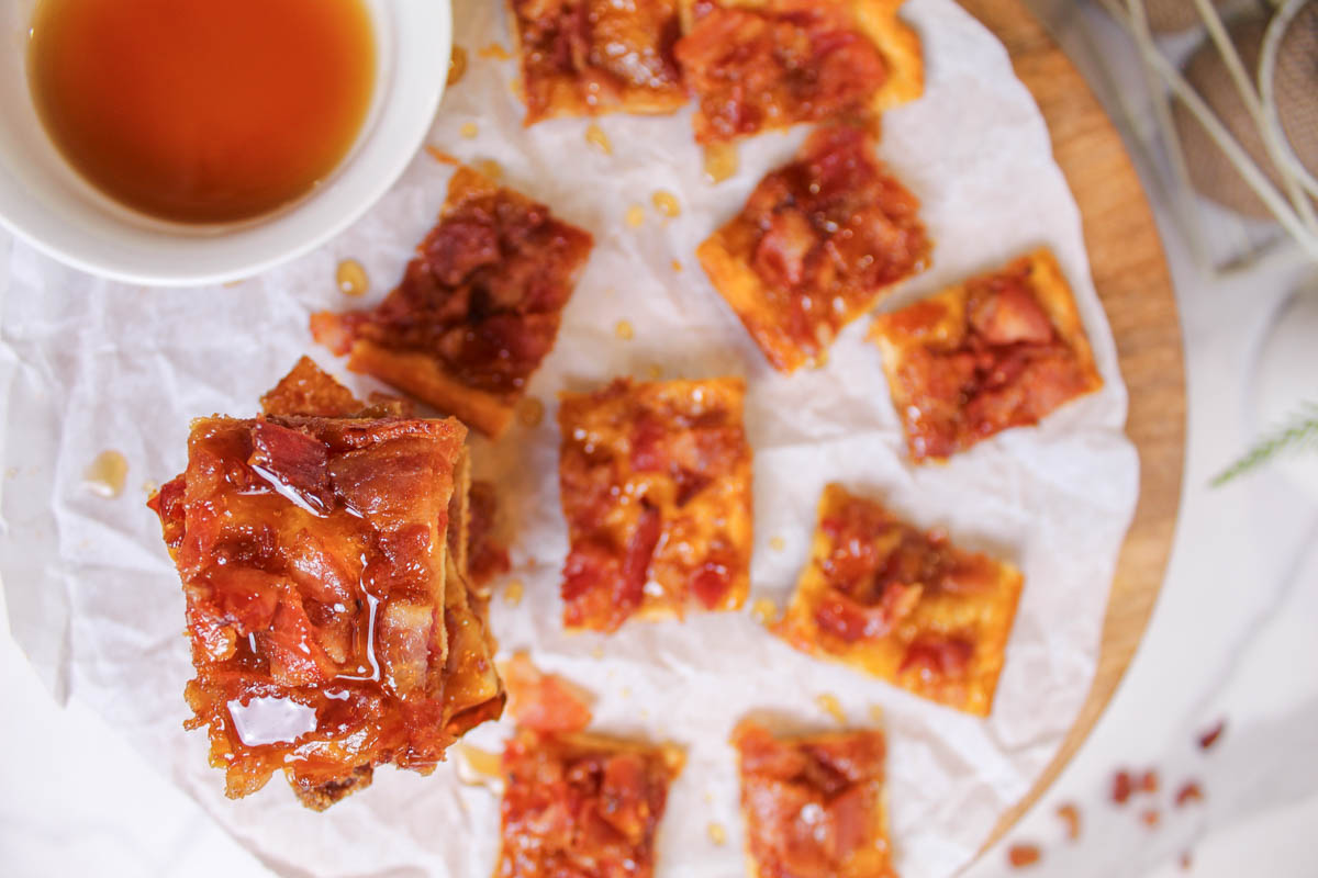 A plate of bacon squares with a bowl of syrup
