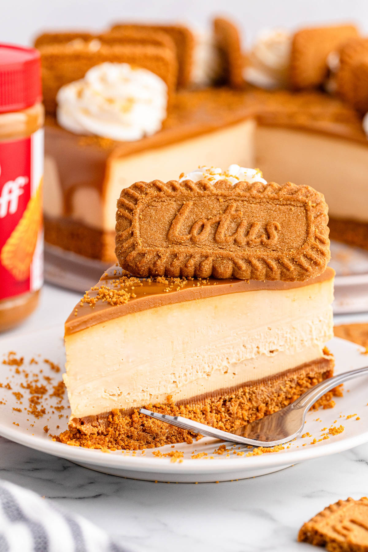 A slice of Biscoff cheesecake on a plate with a jar of Biscoff spread