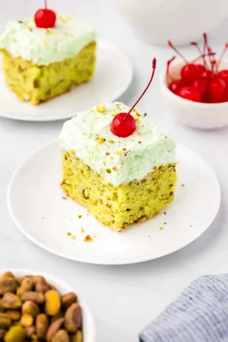 A slice of pistachio cake on a plate with cherries and pistachios, perfect for Christmas celebrations.