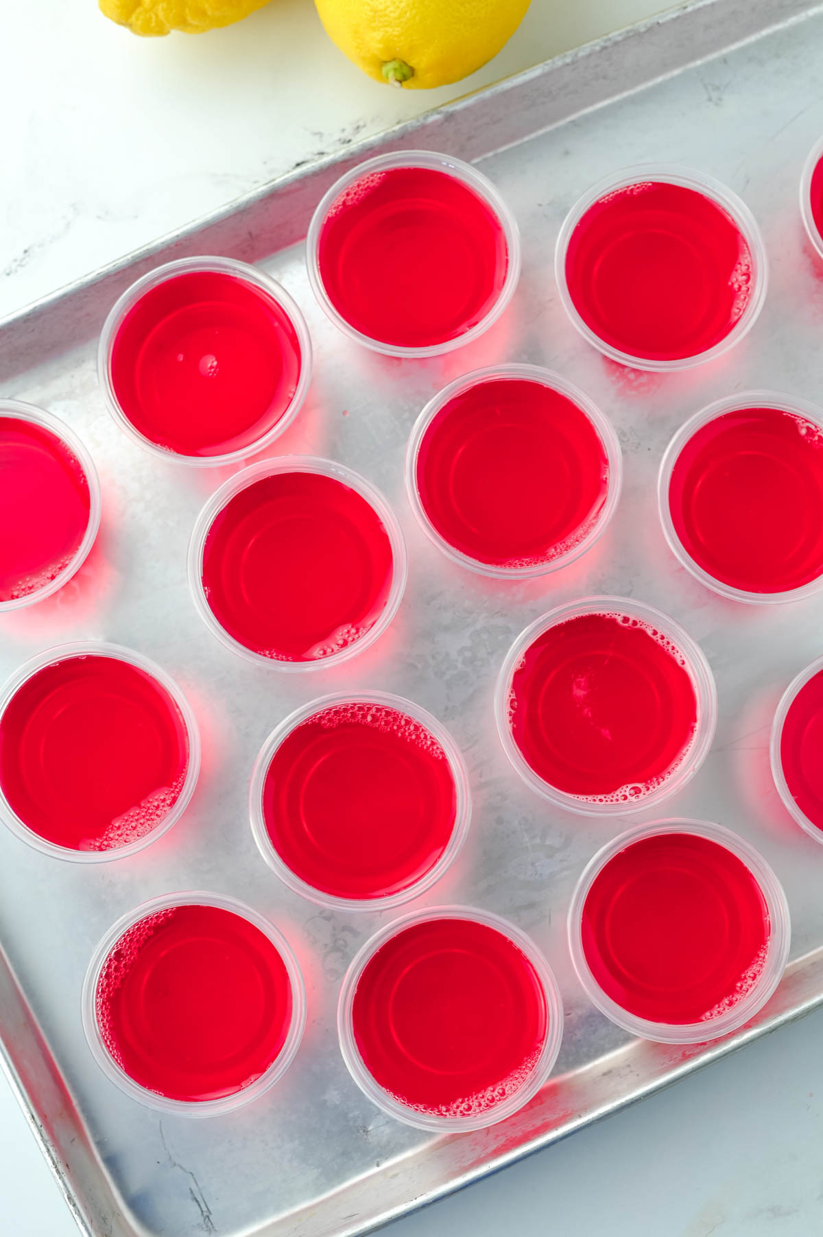 A tray full of red jello shots on a baking sheet.
