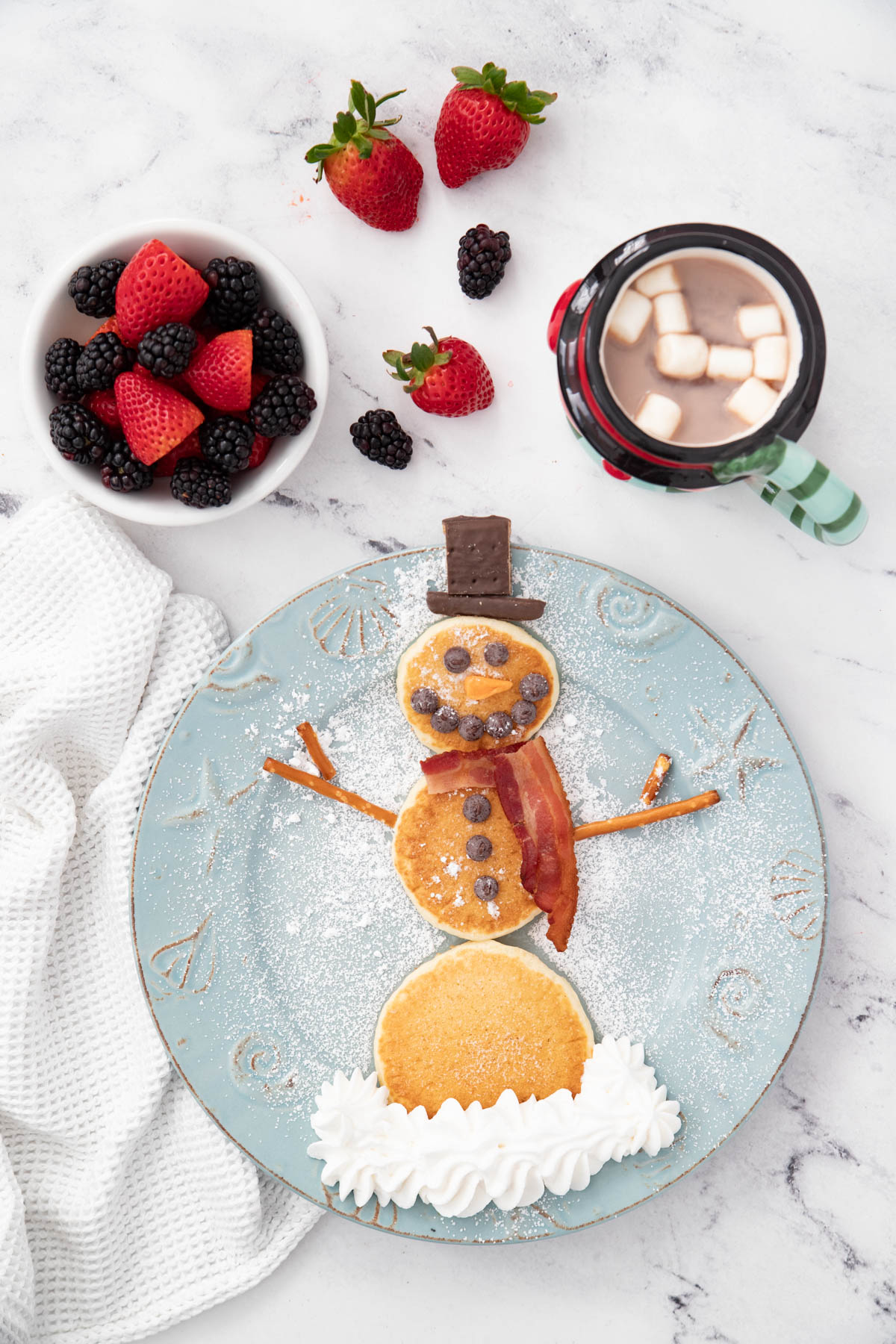 A plate of with a snowman pancake and hot chocolate and fruit