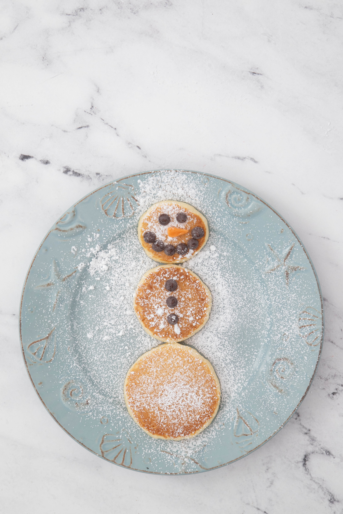 Snowman pancakes with Starburst nose on a plate with powdered sugar.