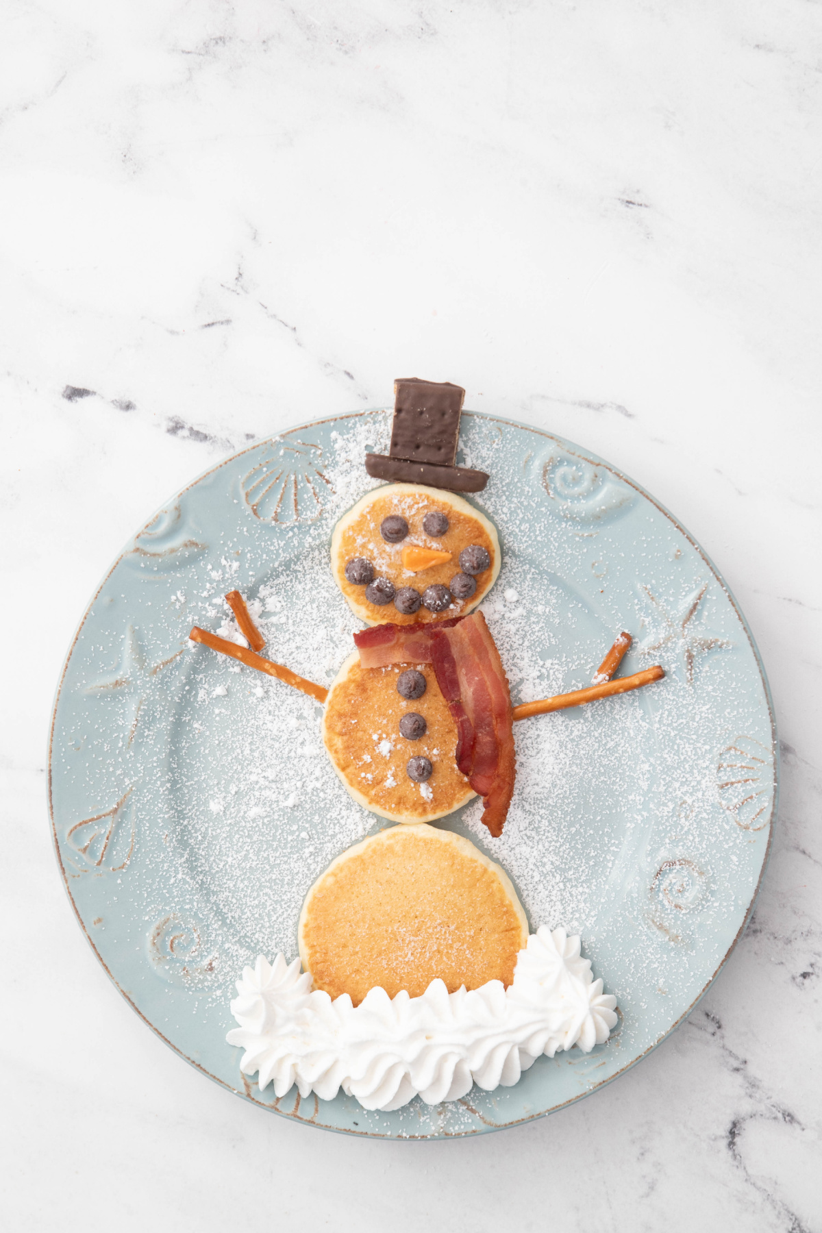 Snowman pancakes with top hat on a plate with powdered sugar.