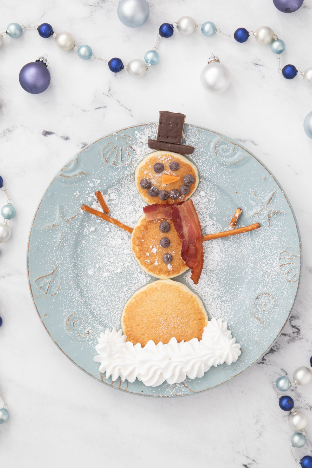 A plate of pancakes in the shape of a snowman surrounded by Christmas decor