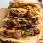A stack of steak quesadillas with peppers on a cutting board.