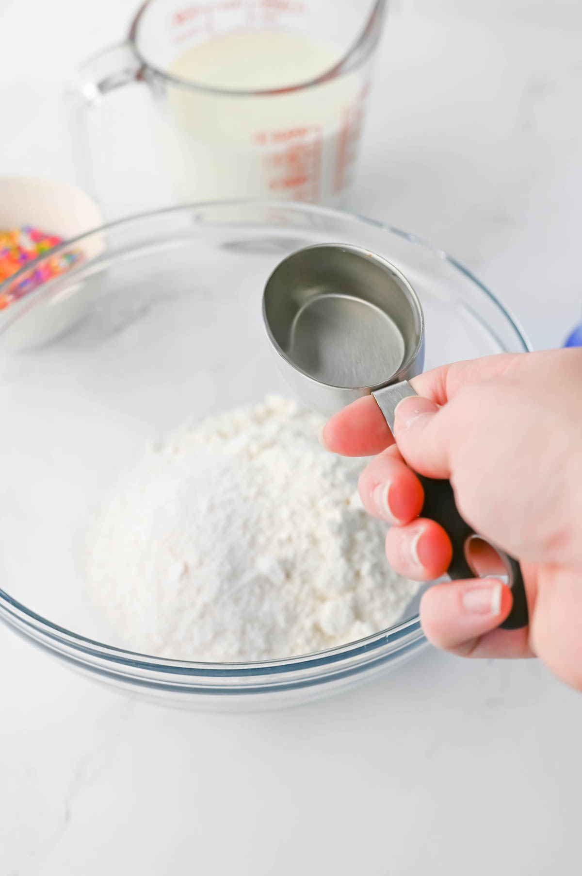 A person is using a measuring spoon to add ingredients in a bowl.
