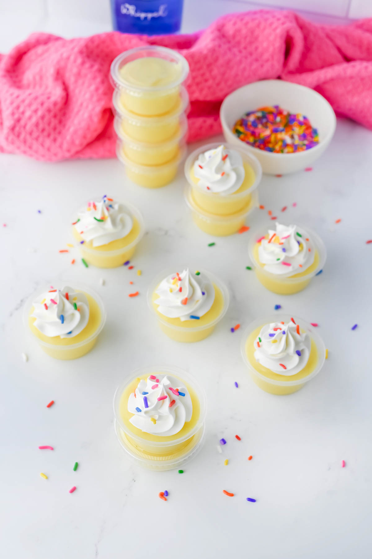 Cupcakes with whipped cream and sprinkles on a white table.