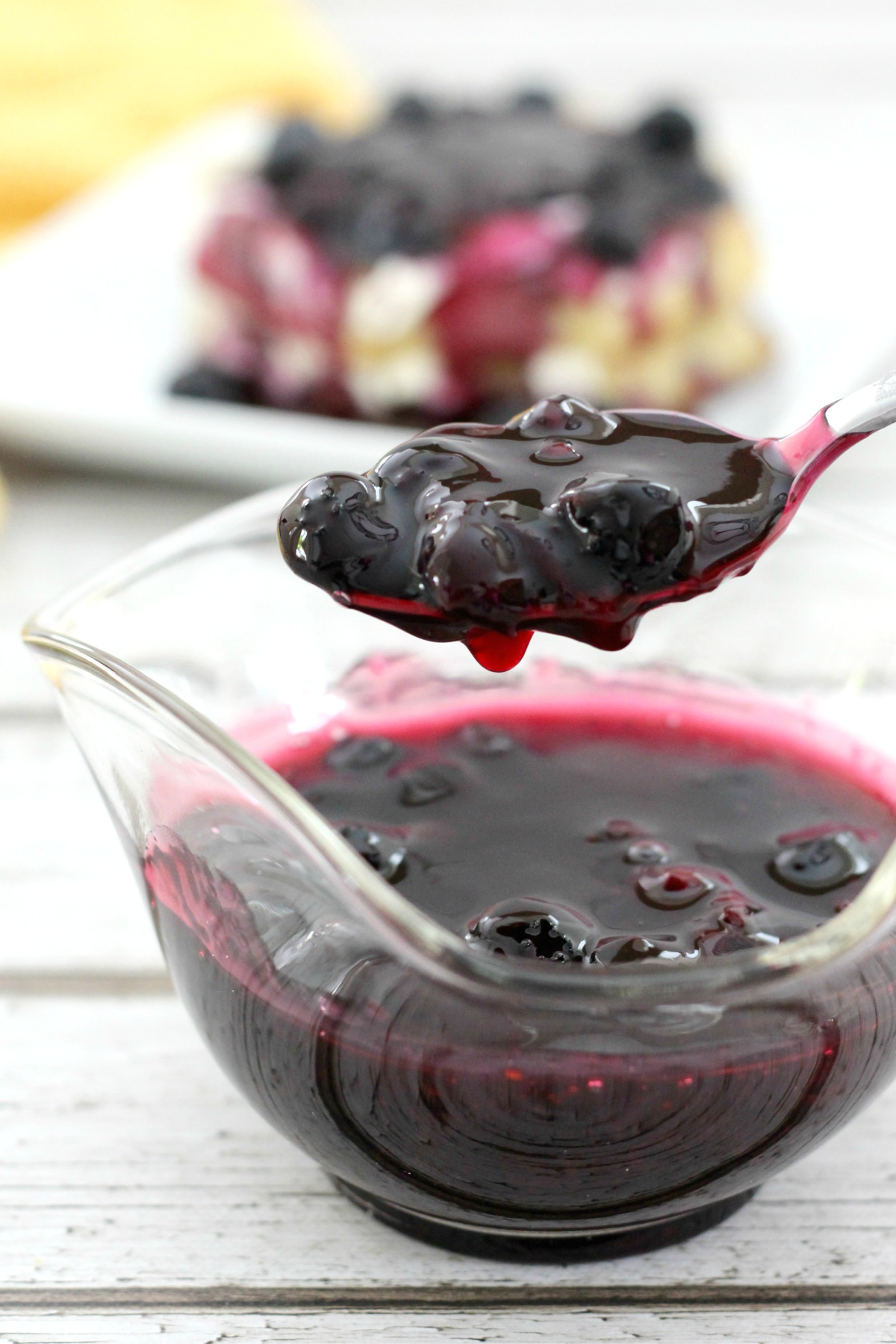 A spoon is being dipped into a bowl of blueberry sauce.