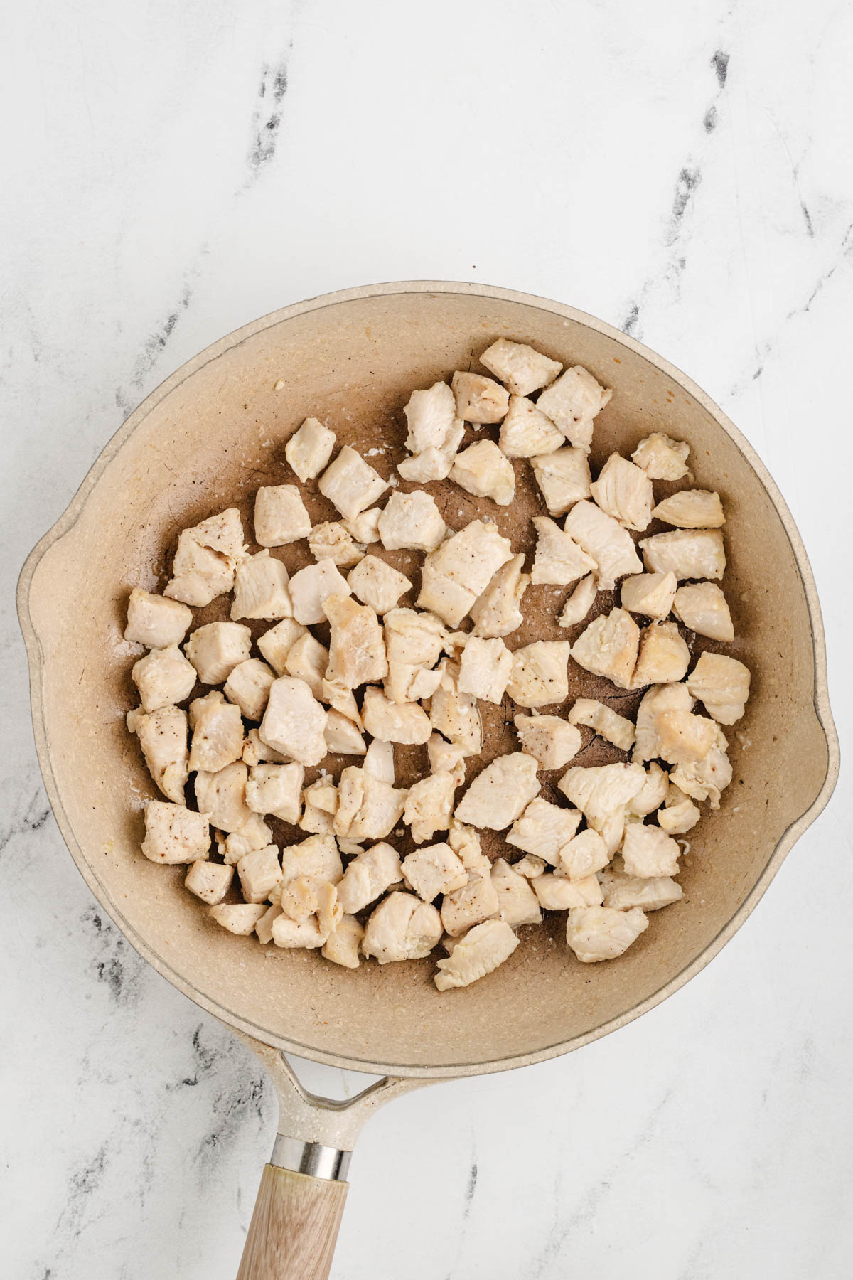 Chicken cubes in a frying pan on a marble countertop.