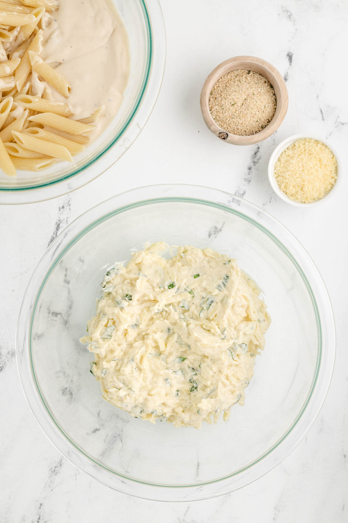 Parmesan and ricotta cheeses, egg and basil next to a bowl of pasta.