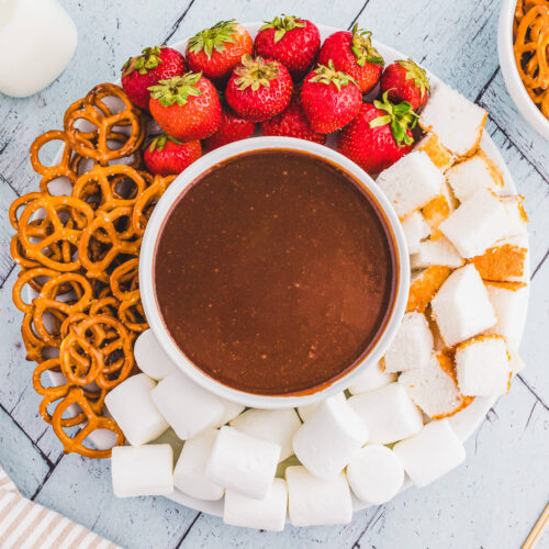 A plate with strawberries, pretzels, chocolate and marshmallows.