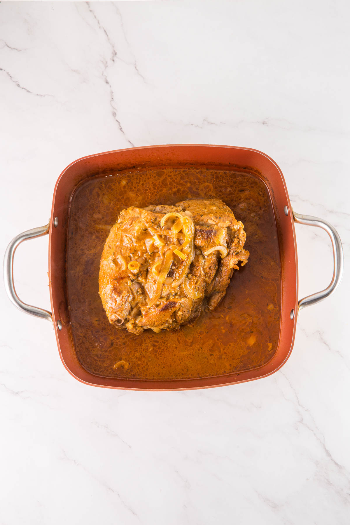 Pork in a red baking dish on a marble countertop.