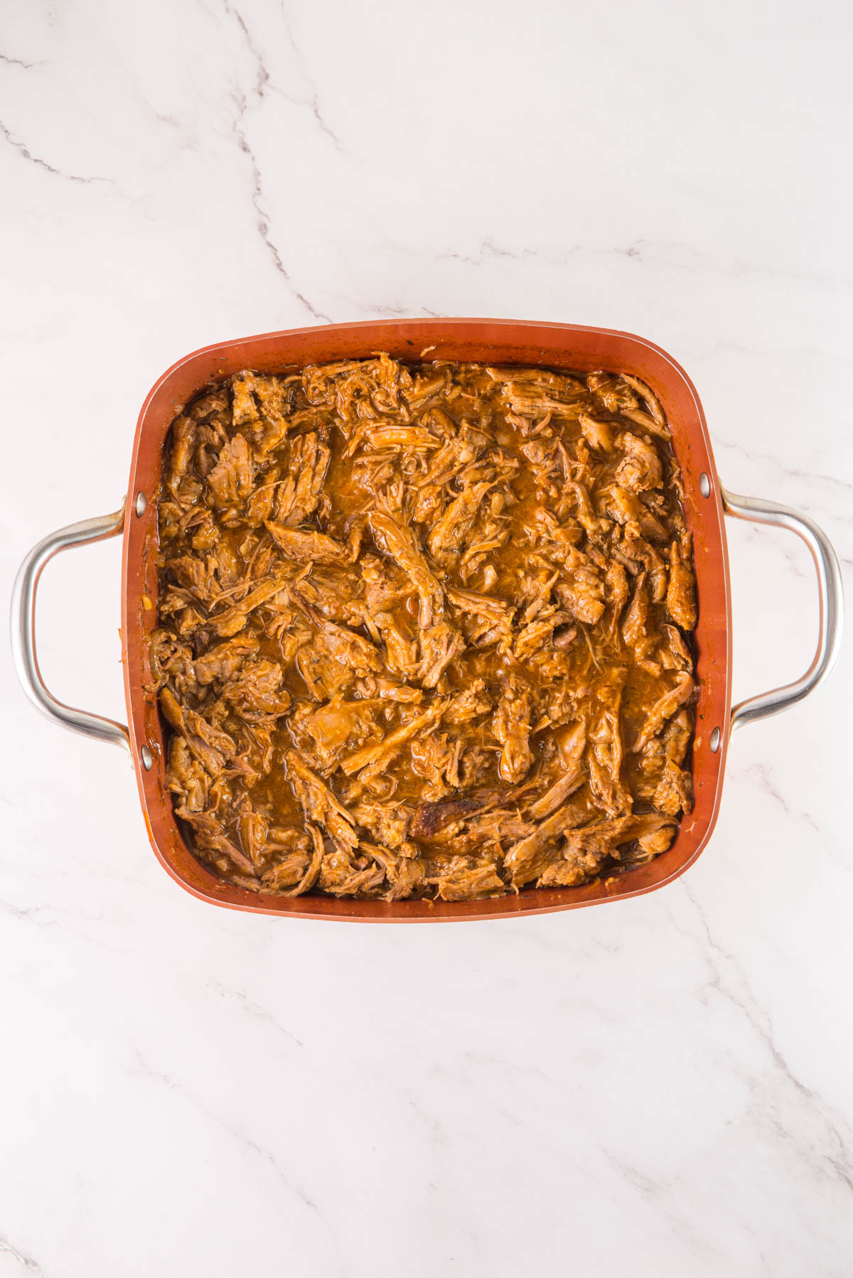 Pulled pork in a red baking dish on a marble countertop.