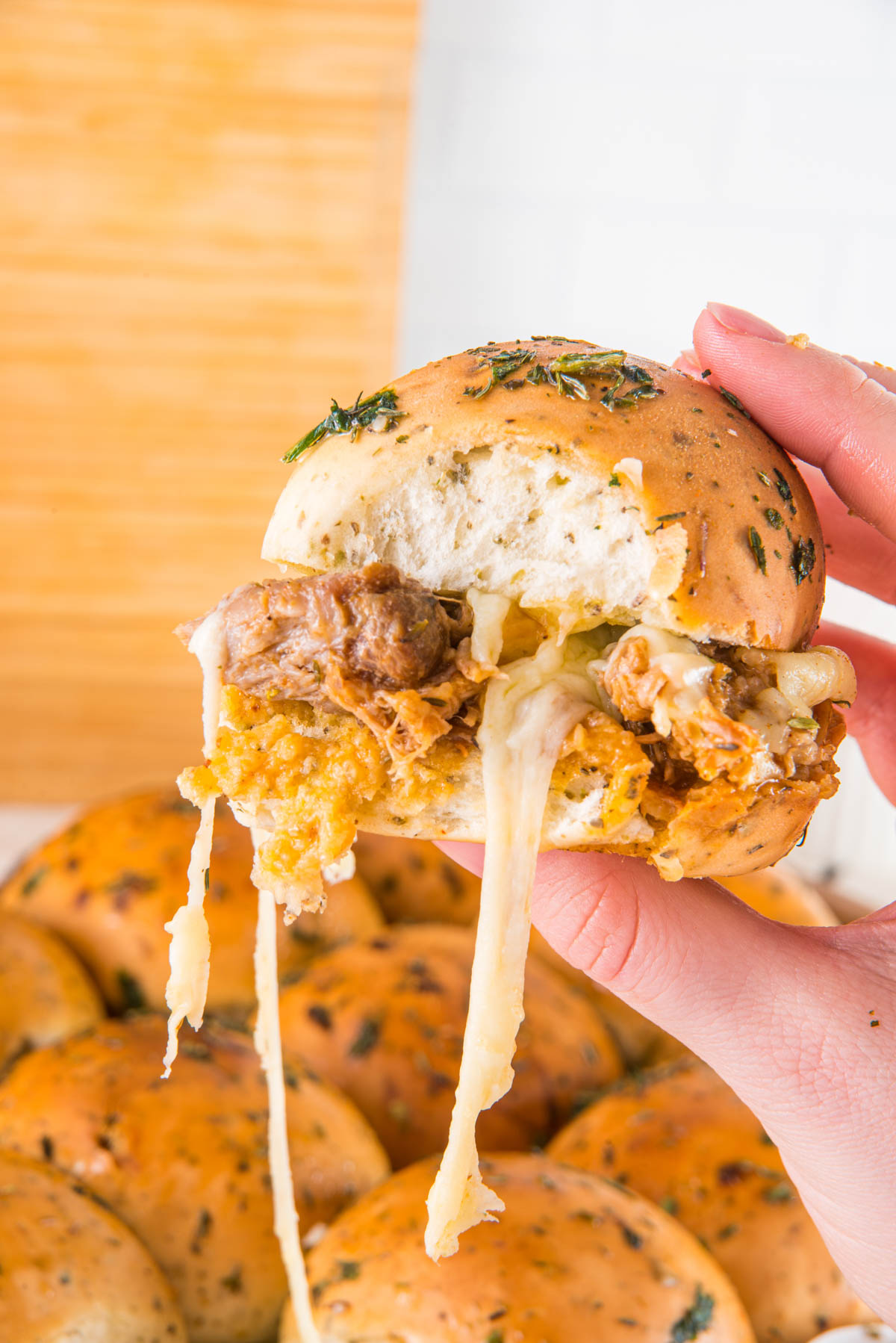A person holding a pulled pork slider with cheese on it.